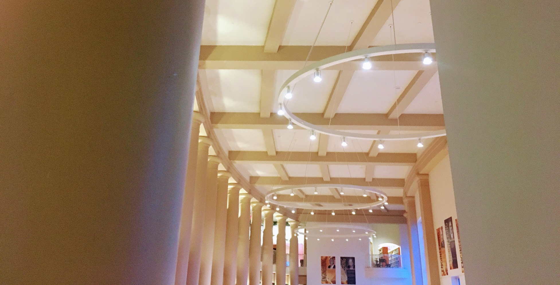 Peeking between
          two walls, you see a vast, curved great hall, with two-story
          columns, large, ring-shaped chandeliers, and a blue glow at
          the far corner of the room.